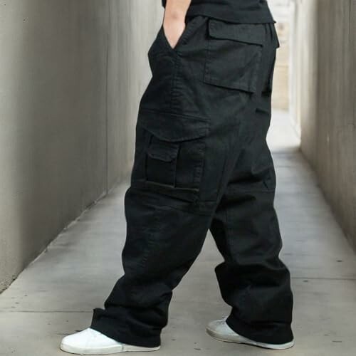 Person wearing baggy black cargo pants and white sneakers in a narrow alley.