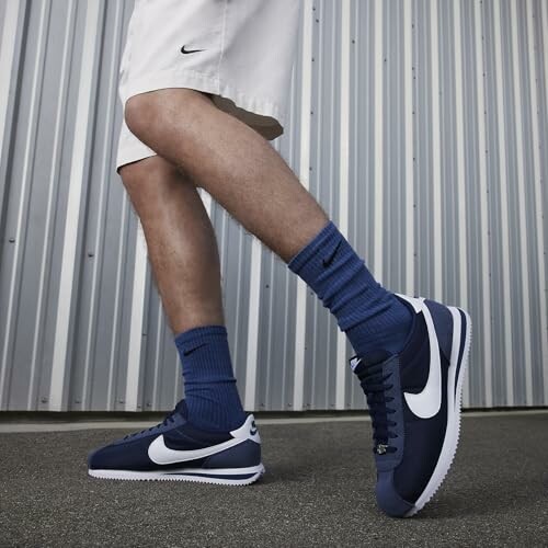 Person wearing blue Nike sneakers and socks walking on pavement.