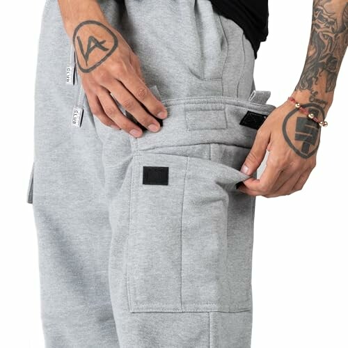 Person wearing grey cargo pants with tattoos on arms.