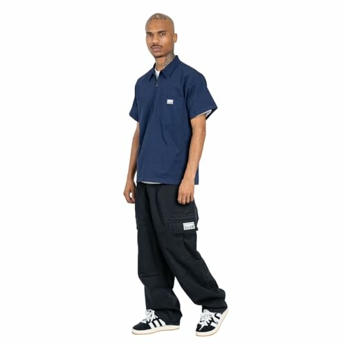 Man wearing a navy shirt and black pants with sneakers.