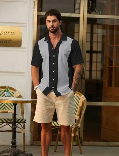 Man in casual shirt and shorts standing outside a cafe.