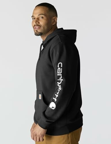 Man wearing black Carhartt hoodie with logo on sleeve.